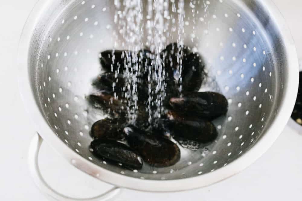 These steamed mussels are easy, elegant, and delicious! They are perfect for any dinner party and you won't be able to stop after just one! Mussels being rinsed with water.