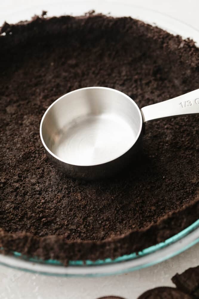 A measuring cup pressing the Oreo crust down.